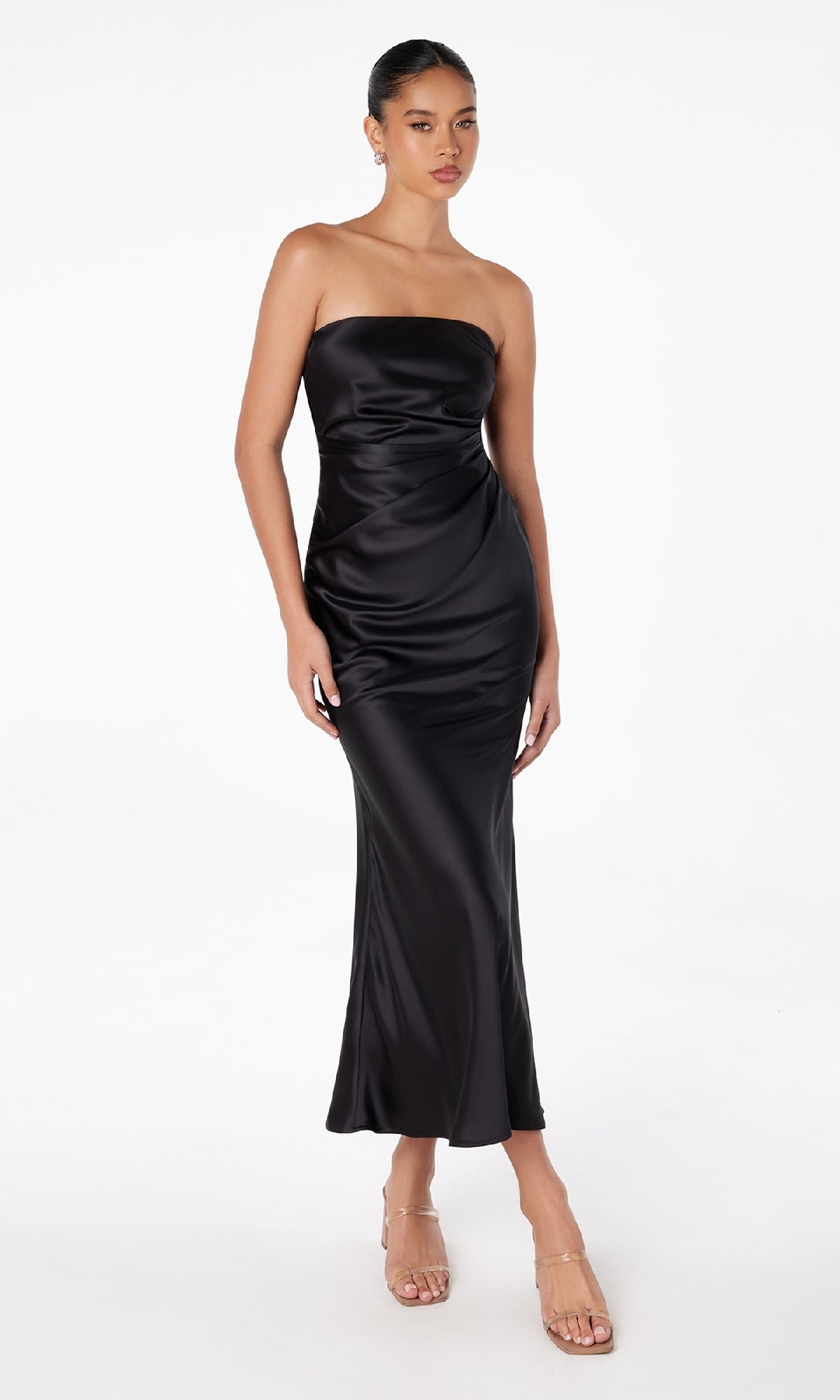 A woman wearing the Strapless Long Satin Maxi Prom Dress: Astee T2006 and clear high-heeled sandals stands against a plain white background.